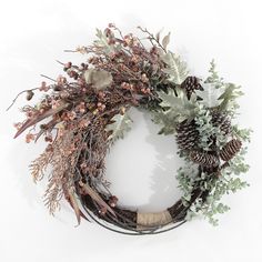 a wreath made out of branches, leaves and pine cones with berries on the side