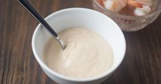 a bowl of shrimp dip next to a plastic cup with shrimp in it on a wooden table