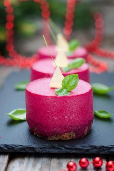 three desserts on a black plate with green leaves