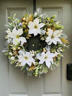 a wreath with white flowers and greenery hanging on a door