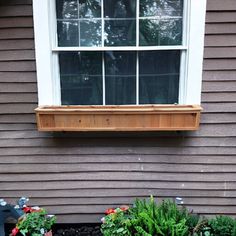 a window sill on the side of a house with flowers in it and plants growing outside