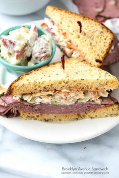 a white plate topped with a cut in half sandwich next to a bowl of cole slaw