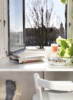 a white chair sitting in front of a window next to a plate of food and drink