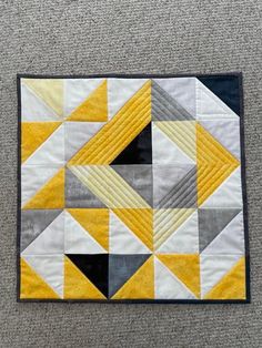 a yellow and grey quilted piece on the floor next to a gray rug with black edges