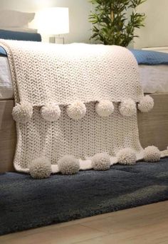 a white crocheted blanket with pom - poms on the edge of a bed