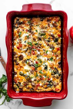 a red casserole dish filled with vegetables and cheese