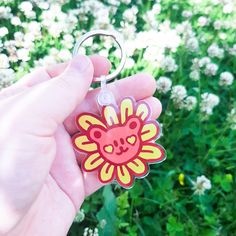 a hand holding a flower shaped keychain in front of some white and green flowers