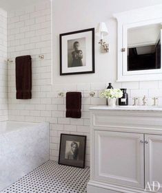 a white bathroom with black and white flooring, framed pictures on the wall above the bathtub