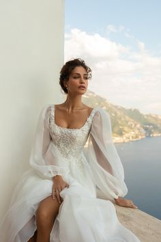 a woman sitting on top of a wall next to the ocean wearing a white dress