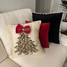 a white couch with christmas pillows on it and a red bow tie around the pillow