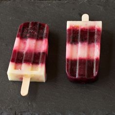 two popsicles with red and white toppings sitting on top of a slate counter