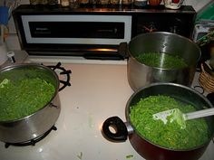 three pans filled with green vegetables on top of a stove next to a microwave