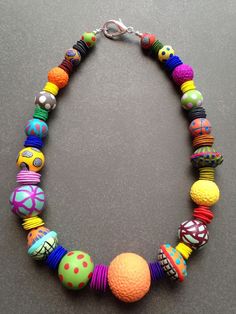 a necklace made with colorful beads on a gray surface and an orange ball hanging from the clasp