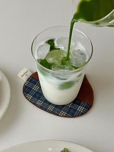 a drink being poured into a glass with ice and green leaves on the rims