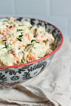 a bowl filled with potato salad on top of a white and black table cloth next to a wooden spoon