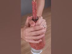 two hands holding a tall glass filled with something red and pink, on top of a wooden table