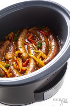 a slow cooker filled with sausages and peppers on top of it's side