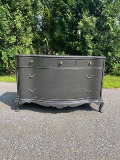 an old dresser is sitting on the pavement in front of some trees and bushes,