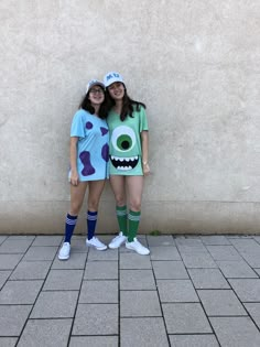 two girls dressed up as monsters standing next to each other in front of a wall