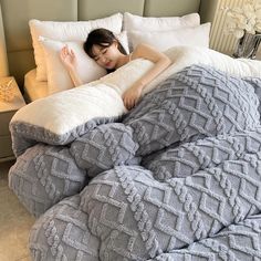 a woman laying in bed with pillows on top of her head and under the covers