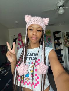 a girl with long braids and a pink hat making the peace sign in front of her