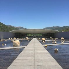 an empty walkway leading to a building with rocks in the water and mountains in the background