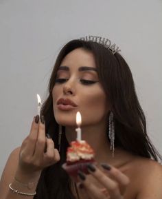 a woman wearing a tiara holding a piece of cake with two candles in it