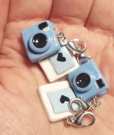 two blue and white square shaped charms with black hearts on them are held in someone's hand