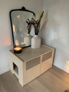 a white vase sitting on top of a wooden table next to a mirror and a lit candle