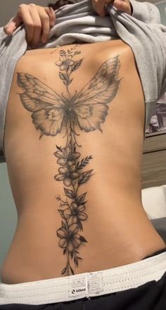 the back of a woman's stomach with flowers and a butterfly tattoo on it