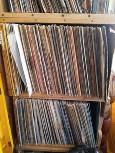 a shelf filled with lots of records next to a yellow bin full of vinyls