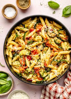 pasta with spinach and tomatoes in a skillet next to other ingredients on a pink surface