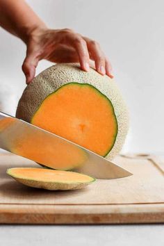 a person is cutting up a melon on a cutting board with a large knife