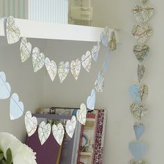 some paper hearts are hanging from the wall next to a vase with flowers in it