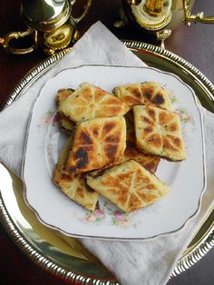 four pieces of food on a plate with silverware and cups in the back ground