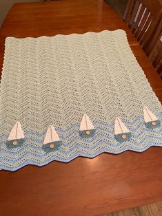 a crocheted tablecloth with sailboats on it sitting on top of a wooden table