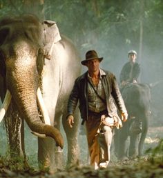 two men are walking with an elephant in the woods while another man stands next to them