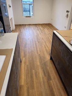 an empty kitchen with hard wood floors and white counter tops in front of a window