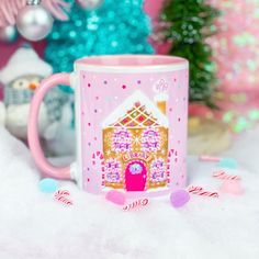 a pink coffee mug with a gingerbread house on the front and candy canes around it