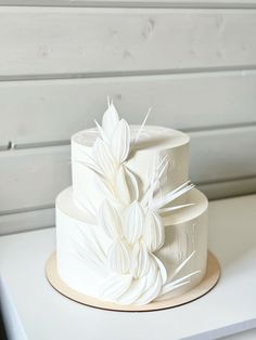 a three tiered cake with white flowers on it sitting on a countertop next to a wall