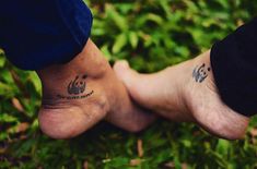 two people with tattoos on their feet standing next to each other in some green grass