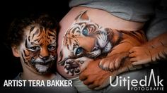 two people with painted faces and body art on their stomachs, one is holding a baby tiger