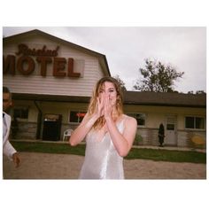 a woman standing in front of a hotel holding her hands to her mouth and looking at the camera