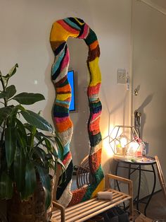 a room with a wooden bench and colorful knitted scarf hanging on the wall next to a potted plant