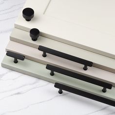 three different colored drawers with black handles and knobs on top of each drawer, sitting on a white marble surface