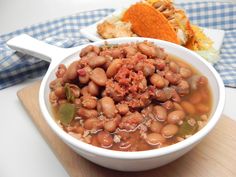 a white bowl filled with lots of beans on top of a wooden cutting board next to a tortilla