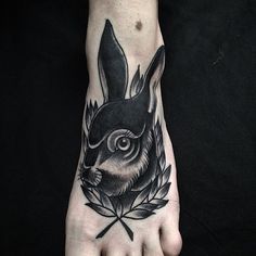 a black and white tattoo of a rabbit on the left foot with leaves around it