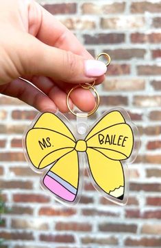 a hand holding a keychain with a yellow bow on it that says, ms ballet