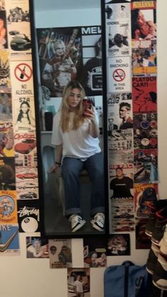 a woman taking a selfie in front of a mirror with posters on the wall