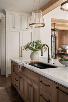 a kitchen with wooden cabinets and marble counter tops, hanging lights over the sink area